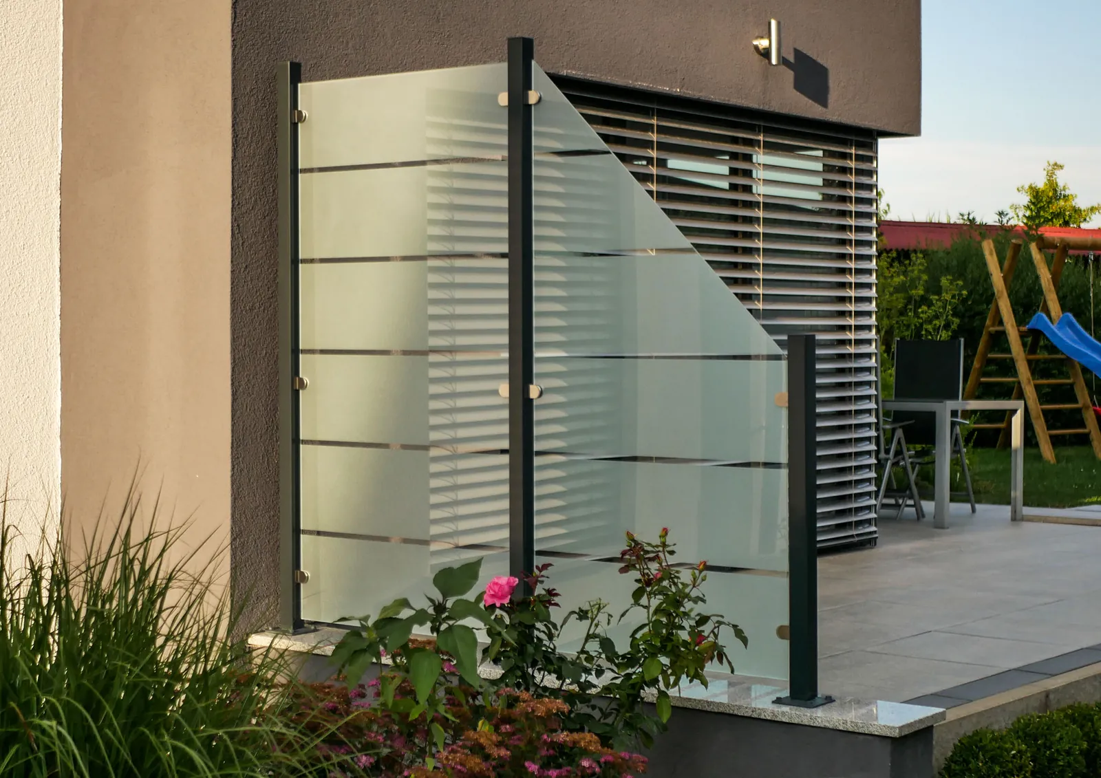 Glaszaun mit Linienmotiv als Sichtschutz neben einer Terrasse