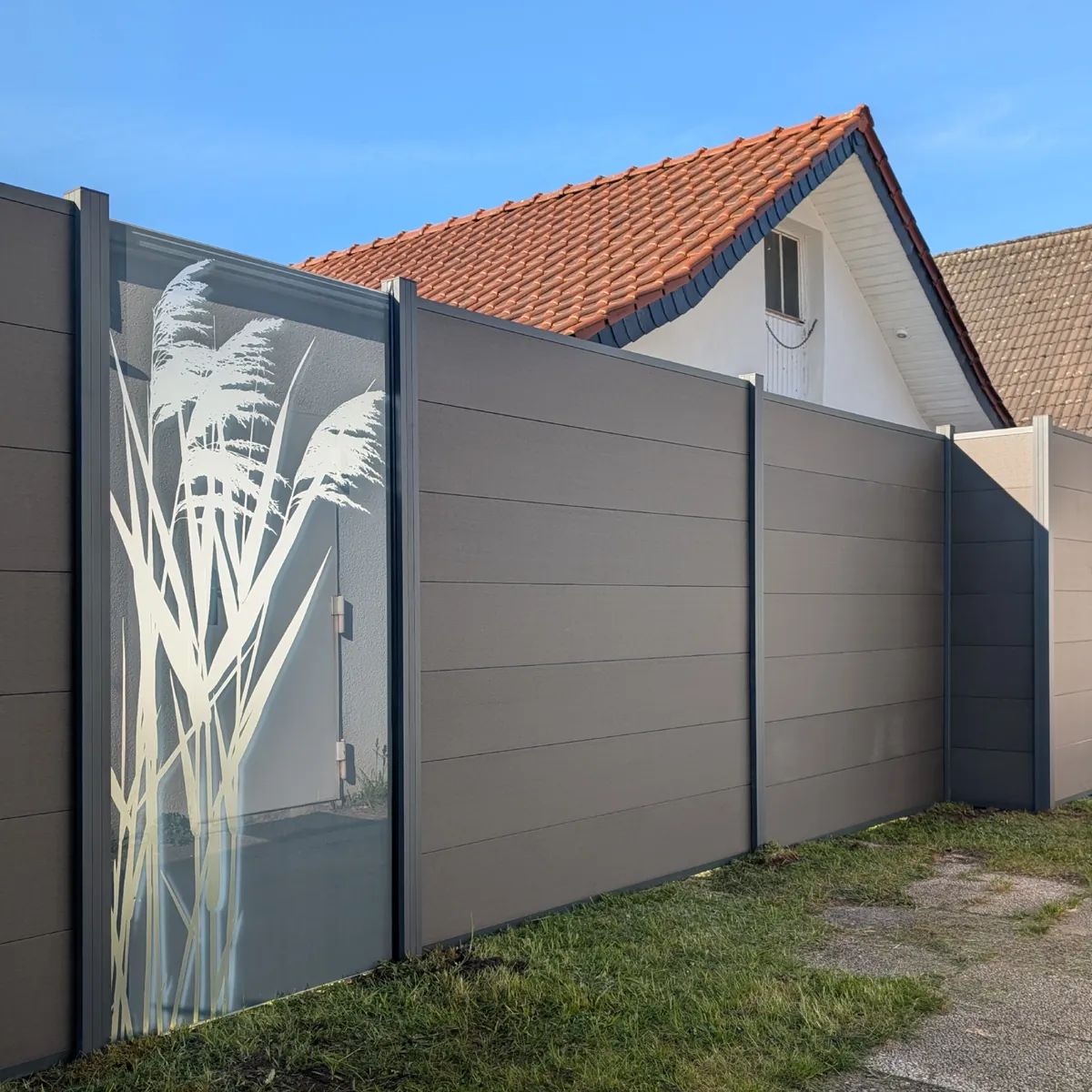 WPC-Zaun in Steingrau, kombiniert mit einem Glasfeld mit Schilfmotiv